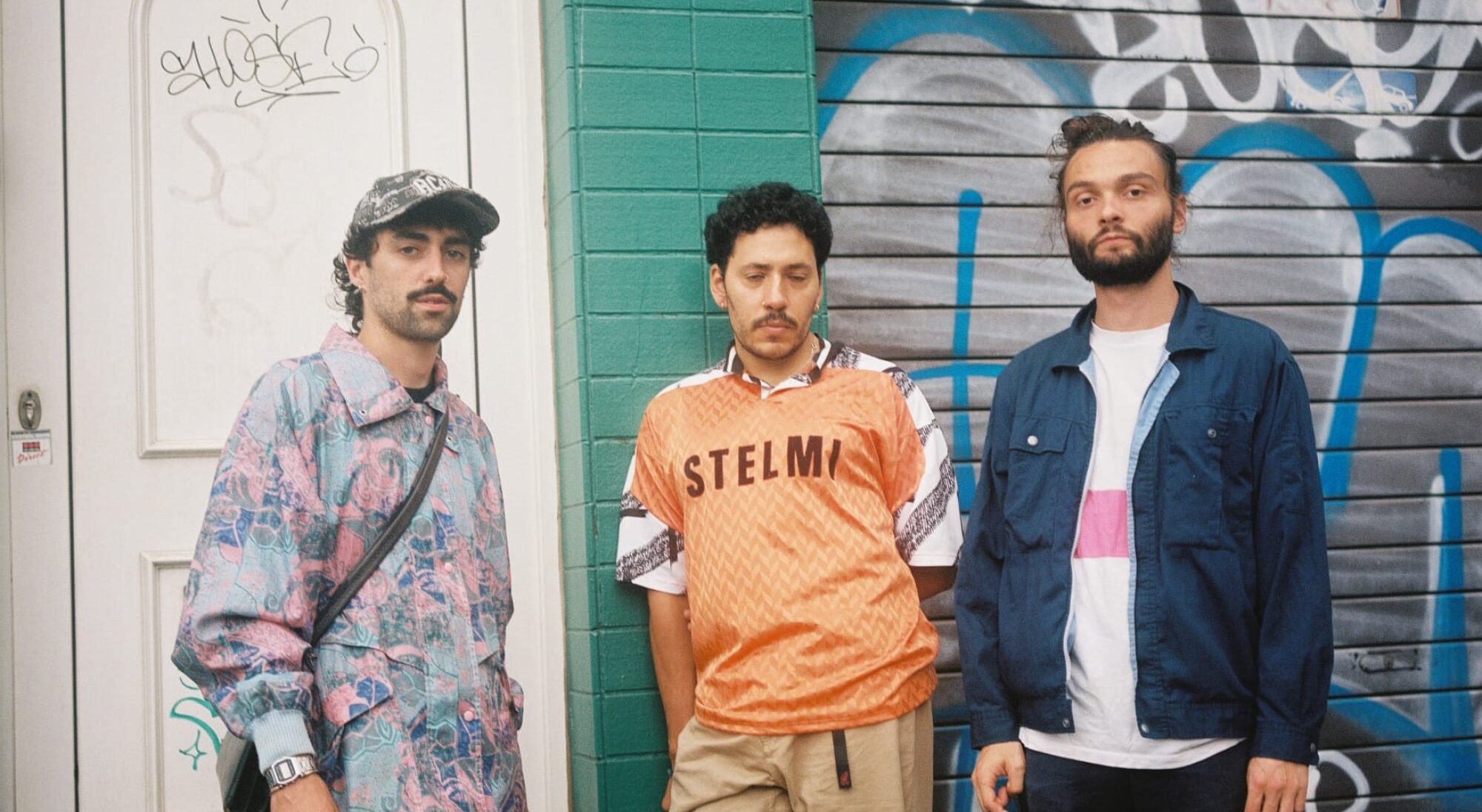 Les trois membres du groupe Floss chillent devant une devanture de maison taguée