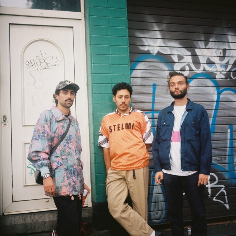 Les trois membres du groupe Floss chillent devant une devanture de maison taguée